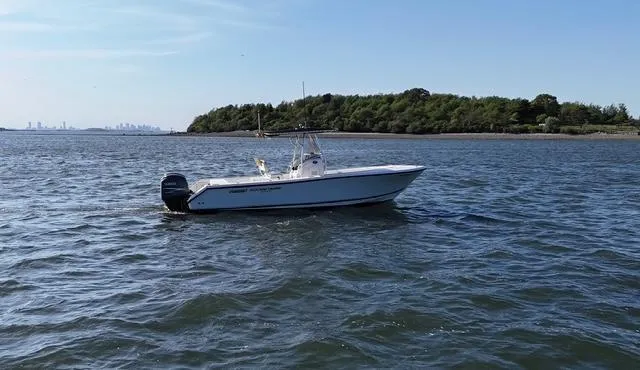 Slide: The Image of 2005 Pursuit 2570 Center Console boat on calm water near a wooded shoreline. - 8