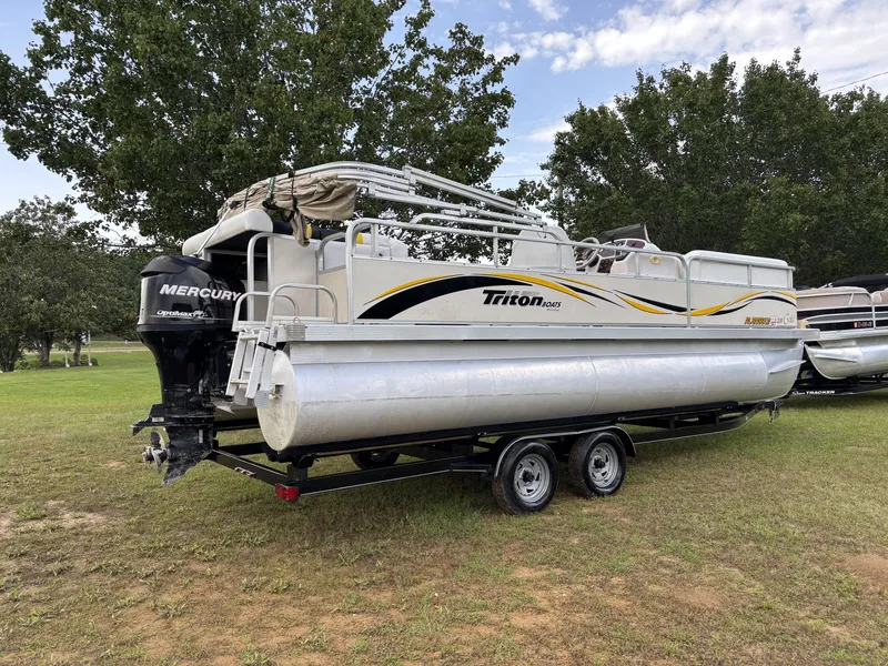 Slide: The Image of 2007 Triton 220 Gold pontoon boat with Mercury engine on a trailer, parked on grass. - 7