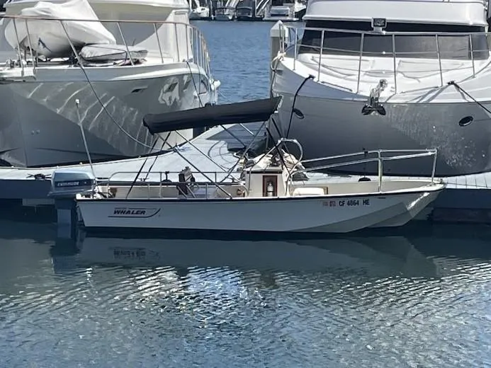 Slide: The Image of 1983 Boston Whaler 17 Montauk boat docked between larger yachts in a marina. - 11