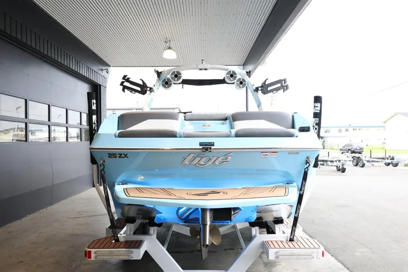 Slide: The Image of 2022 Tigé 25ZX boat, rear view, blue color, parked indoors on a trailer. - 6