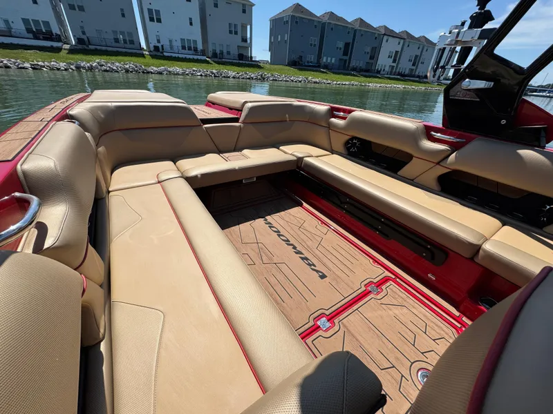 Slide: The Image of 2022 Moomba Makai boat interior with tan seating and red accents, docked near waterfront homes. - 18