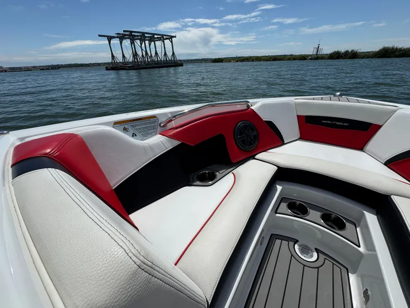 Slide: The Image of 2018 Nautique Super Air Nautique 210 boat interior with red and white seating on a sunny day. - 11