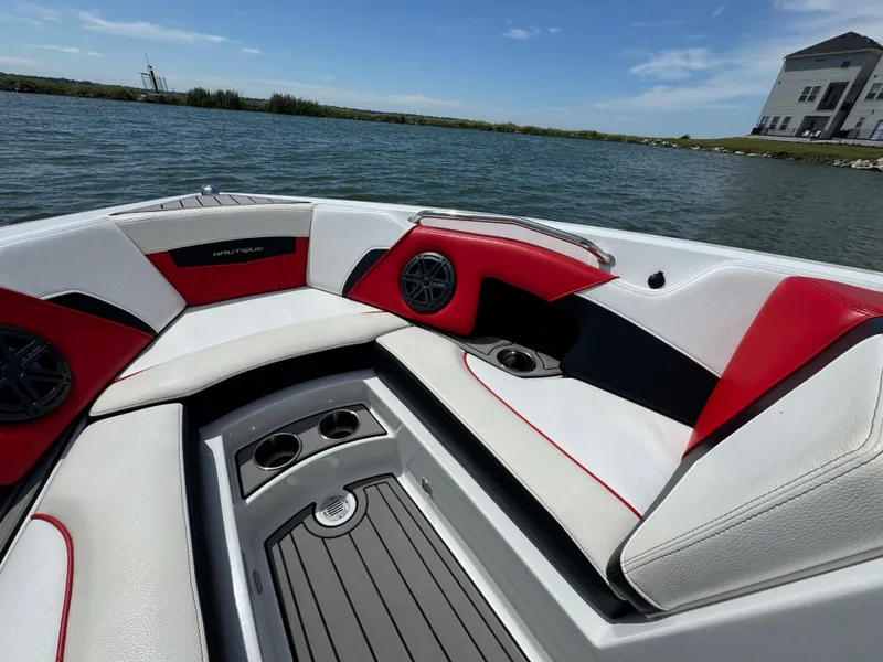Slide: The Image of 2018 Nautique Super Air Nautique 210 boat interior with red and white seating on a lake. - 12