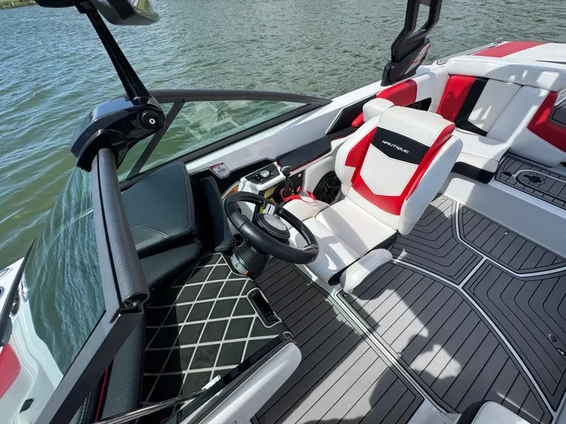 Slide: The Image of 2018 Nautique Super Air Nautique 210 boat interior with red and white seating, steering wheel, and water view. - 14