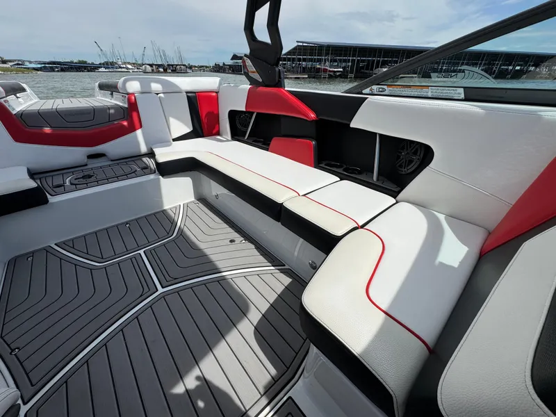 Slide: The Image of 2018 Nautique Super Air Nautique 210 interior with red and white seating, docked by the water. - 16