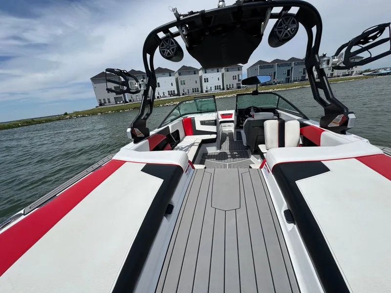 Slide: The Image of 2018 Nautique Super Air Nautique 210 boat interior with red and white seating on a lake. - 20