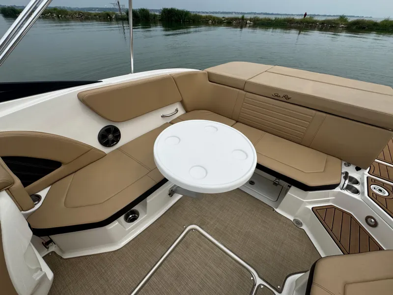 Slide: The Image of 2019 Sea Ray SPX 230 boat interior with tan seating and round table on calm water. - 15