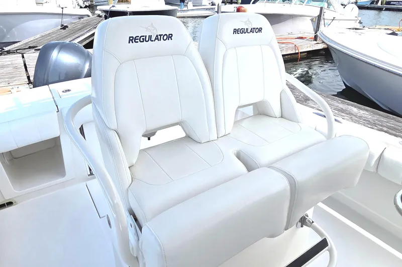 Slide: The Image of 2014 Regulator 28 Forward Seating boat with white cushioned seats at a marina. - 9