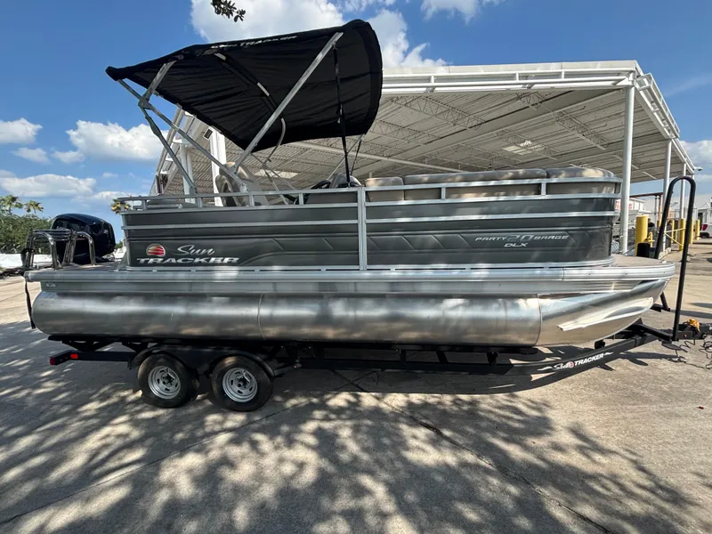 The Image of 2025 Sun Tracker Party Barge 20 DLX pontoon boat on trailer under canopy. - 0