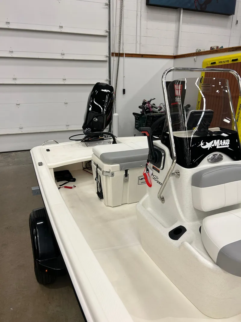 Slide: The Image of 2025 Mako Pro Skiff 15 CC boat in a garage, featuring a center console and seating. - 4