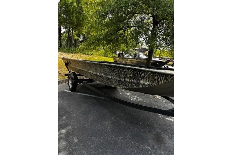 The Image of 2025 Tracker Grizzly 1860 Utility boat on trailer, parked outdoors under trees. - 0