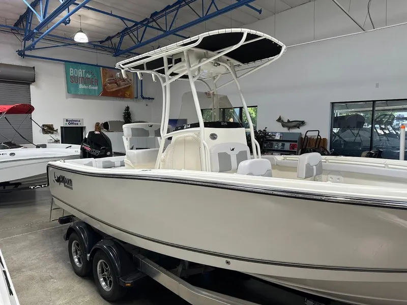 Slide: The Image of 2025 Mako 214 CC boat displayed in showroom, featuring sleek design and dual-axle trailer. - 2