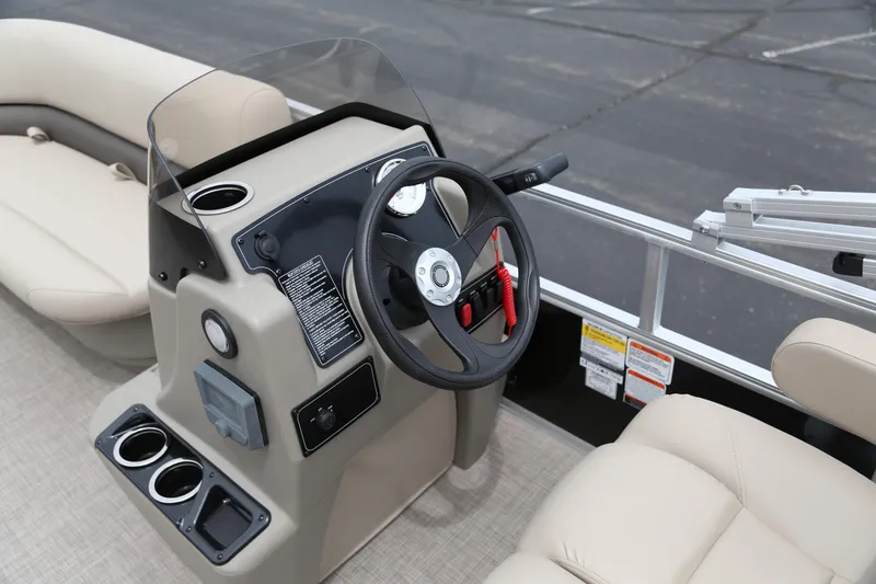 Slide: The Image of 2025 Sun Tracker Party Barge 16 DLX steering console with beige seating and cup holders. - 48