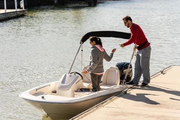 Slide: The Image of 2025 Boston Whaler 130 SUPERSPORT docked with two people, one boarding, on a sunny day. - 2