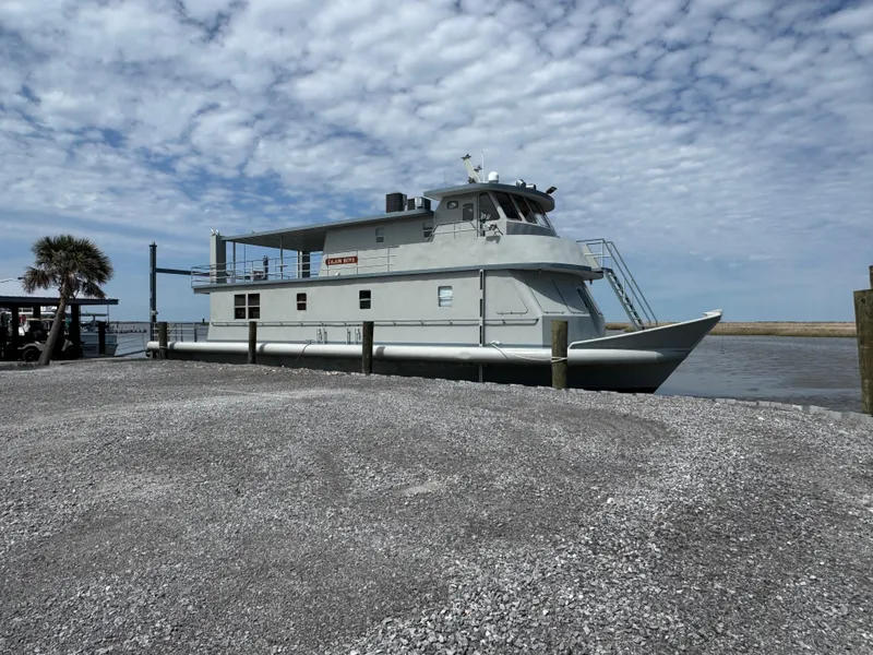 The Image of Custom 1985 houseboat docked by gravel shore under cloudy sky. - 1