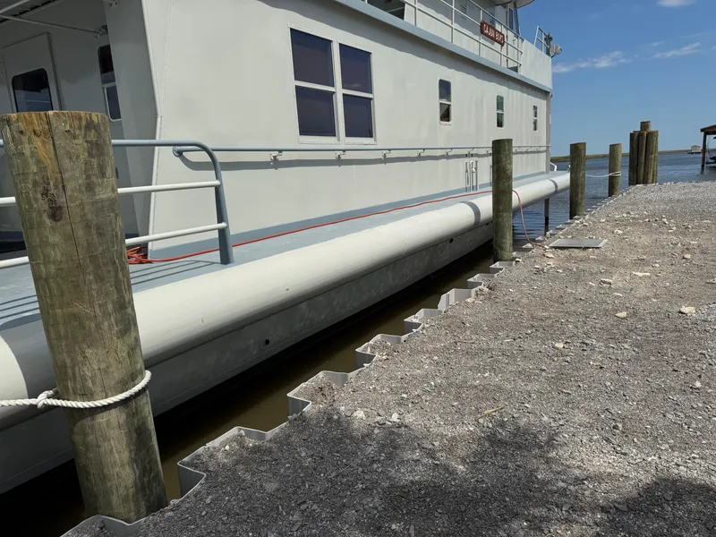 Slide: The Image of Custom 1985 houseboat docked beside a gravel shoreline under a clear blue sky. - 4