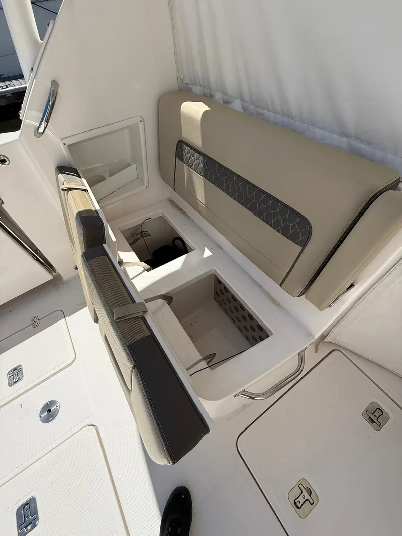 Slide: The Image of 2018 Pursuit DC 365 Dual Console boat interior with beige seating and storage compartments. - 10