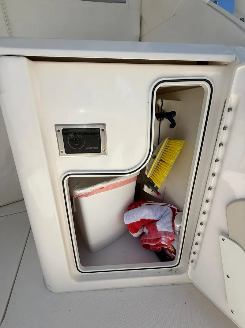 Slide: The Image of Storage compartment on a 2018 Pursuit DC 365 Dual Console boat with cleaning supplies. - 6