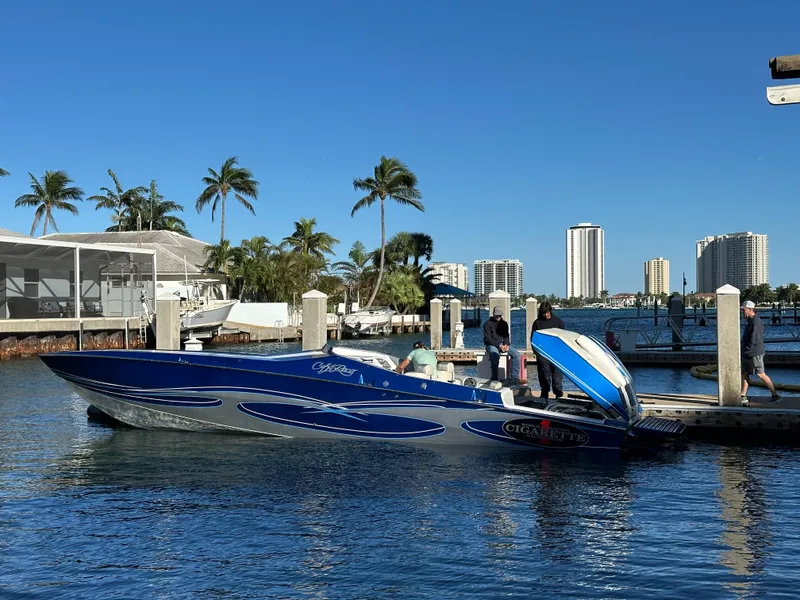 Slide: The Image of 1989 Cigarette 35 Cafe Racer boat docked, with palm trees and city skyline in the background. - 3