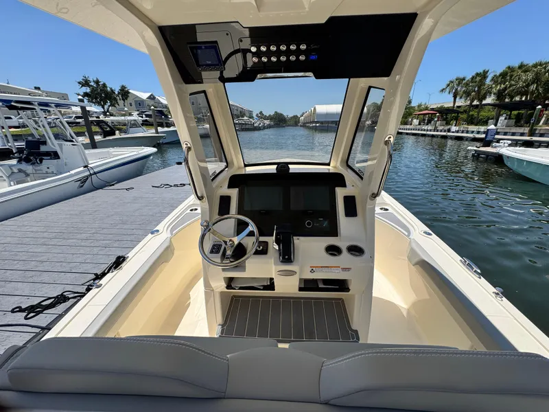 Slide: The Image of 2025 Scout 281 XSS boat cockpit with steering wheel and control panel, docked by a scenic waterfront. - 11