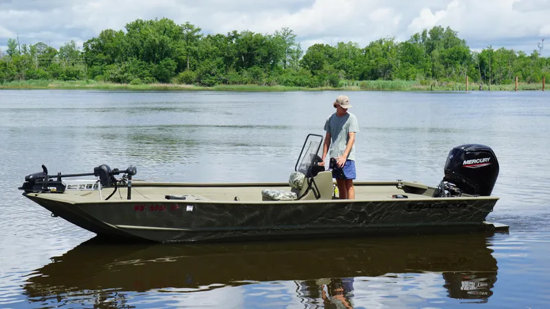 Slide: The Image of 2024 Tracker Grizzly 2072 SC boat on a calm lake with a person standing. - 3