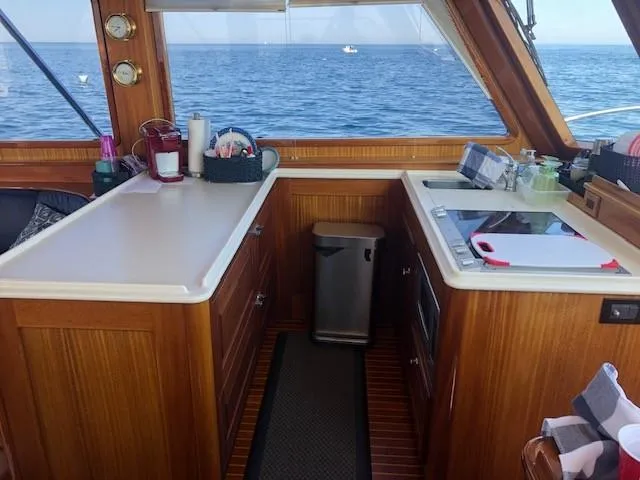 Slide: The Image of 2003 Lyman-Morse Wesmac Sportfish Cruiser interior with ocean view, featuring a compact kitchen area. - 7