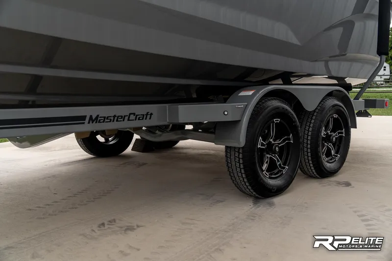 Slide: The Image of 2025 MasterCraft X22 boat trailer with dual axles and sleek black wheels. - 26
