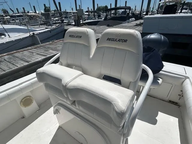Slide: The Image of 2013 Regulator 26 FS boat with dual white cushioned seats at a marina. - 6