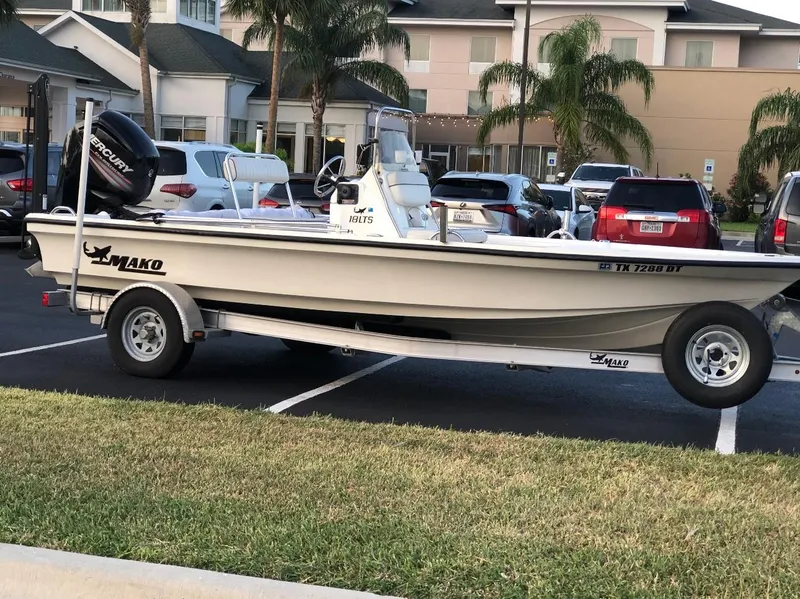 The Image of 2016 Mako 18 LTS boat on trailer in parking lot, surrounded by cars and palm trees. - 0