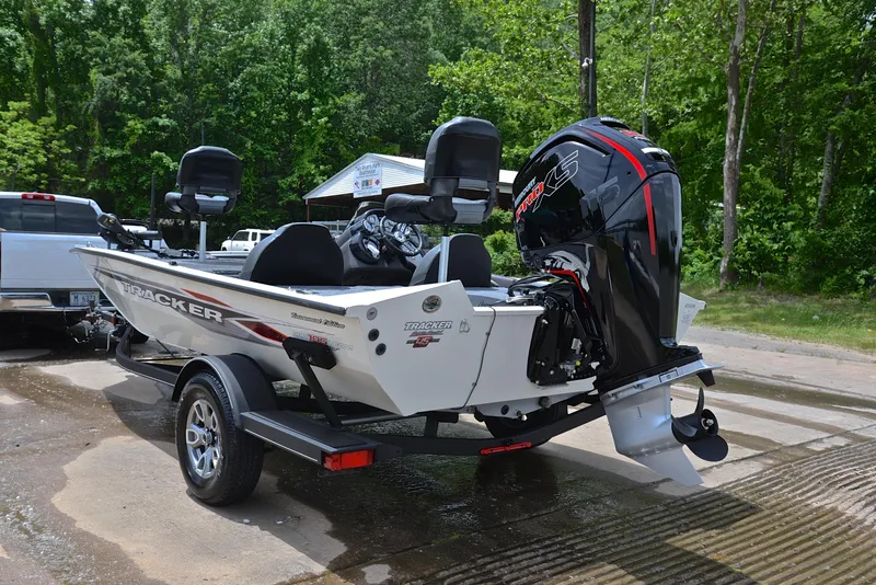 Slide: The Image of 2023 Bass Tracker Pro Team 195 TXE boat on trailer, parked near a forested area. - 12