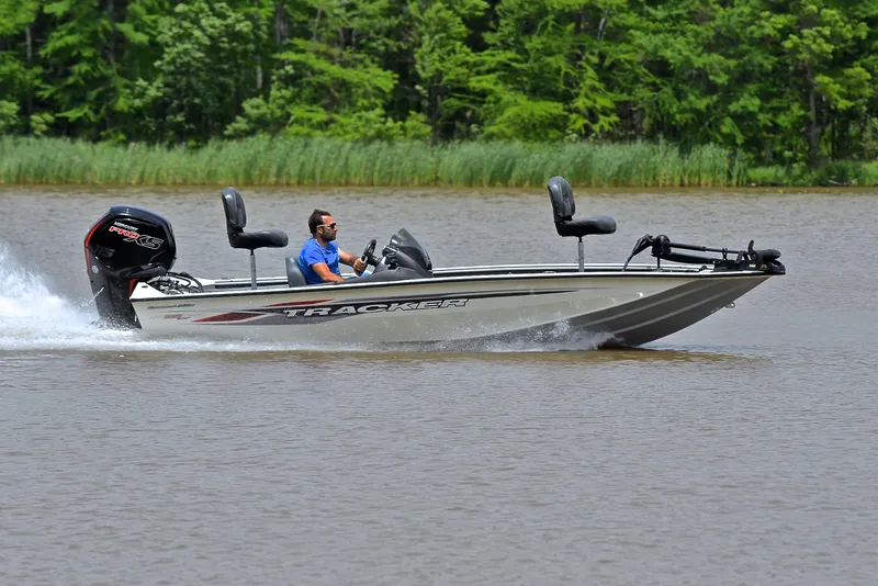 Slide: The Image of 2023 Bass Tracker Pro Team 195 TXE boat speeding on a lake with lush green background. - 3