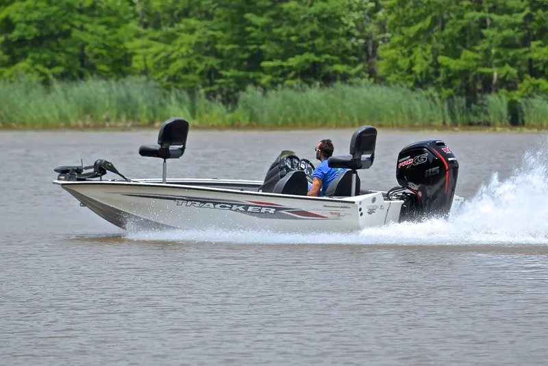 Slide: The Image of 2023 Bass Tracker Pro Team 195 TXE boat speeding on a lake with lush greenery. - 4