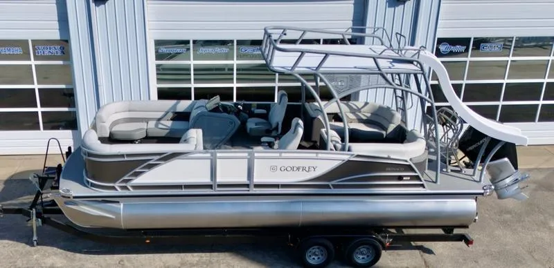 Slide: The Image of 2025 Godfrey Monaco Sundeck 235 SD pontoon boat on trailer, parked outside garage. - 12