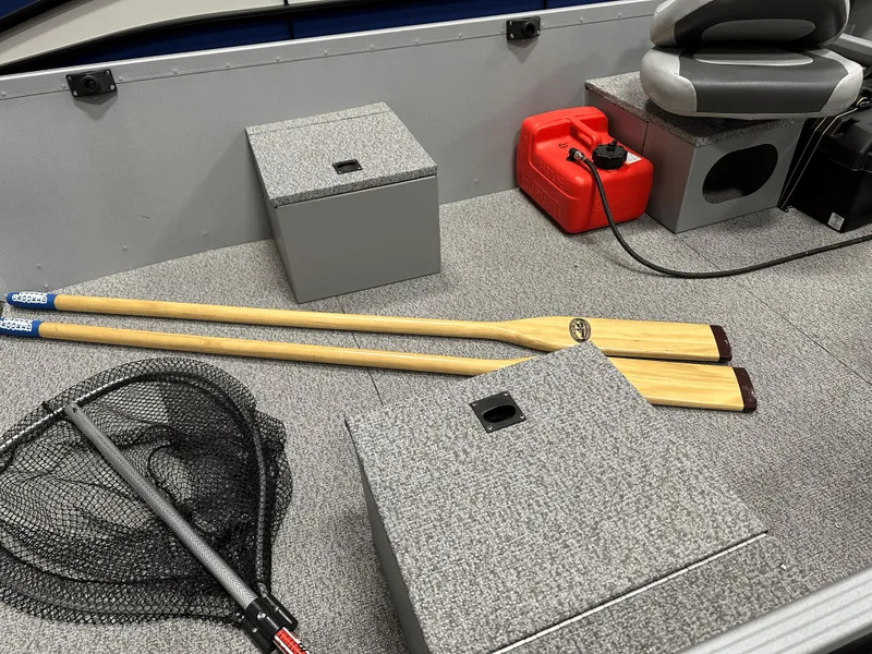Slide: The Image of 2023 Alumacraft V14 boat interior with oars, fishing net, and fuel tank. - 10