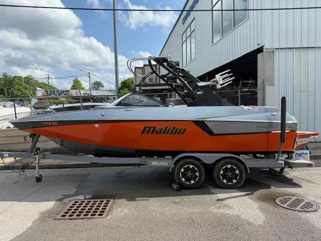 Slide: The Image of 2019 Malibu Wakesetter 22 MXZ boat on trailer, orange and gray, parked outdoors. - 1