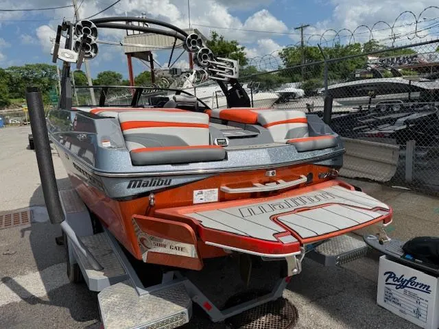 Slide: The Image of 2019 Malibu Wakesetter 22 MXZ boat on trailer, orange and gray design, parked outdoors. - 3