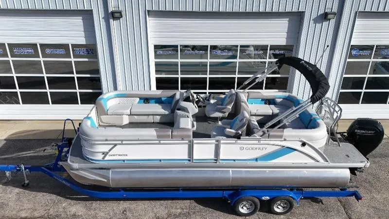 Slide: The Image of 2025 Godfrey Sweetwater 2286 SB pontoon boat on trailer, parked outside a building. - 1