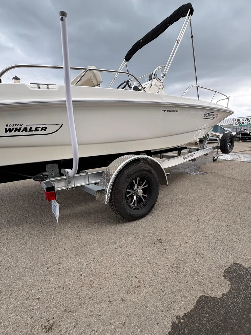 Slide: The Image of 2019 Boston Whaler 170 Dauntless boat on trailer, parked on pavement under cloudy sky. - 18