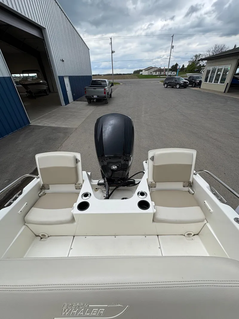 Slide: The Image of 2019 Boston Whaler 170 Dauntless boat interior with seating and motor, parked outdoors. - 8