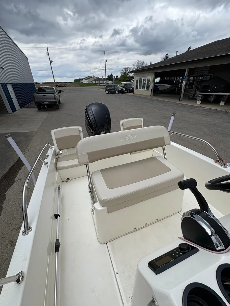 Slide: The Image of 2019 Boston Whaler 170 Dauntless boat with seating and controls, parked outdoors. - 9
