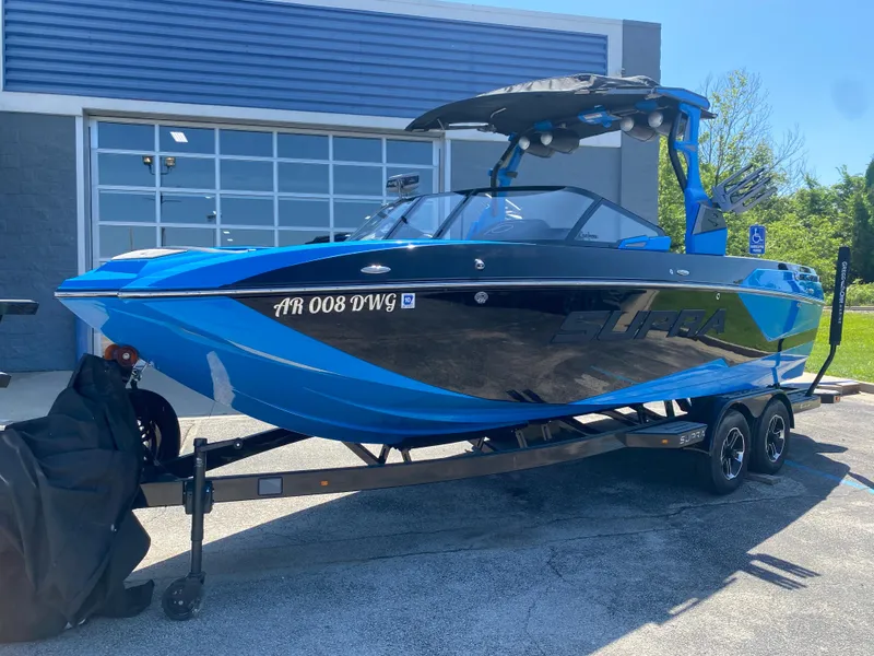 Slide: The Image of 2021 Supra SL 450 boat in blue and black on a trailer outside a garage. - 0