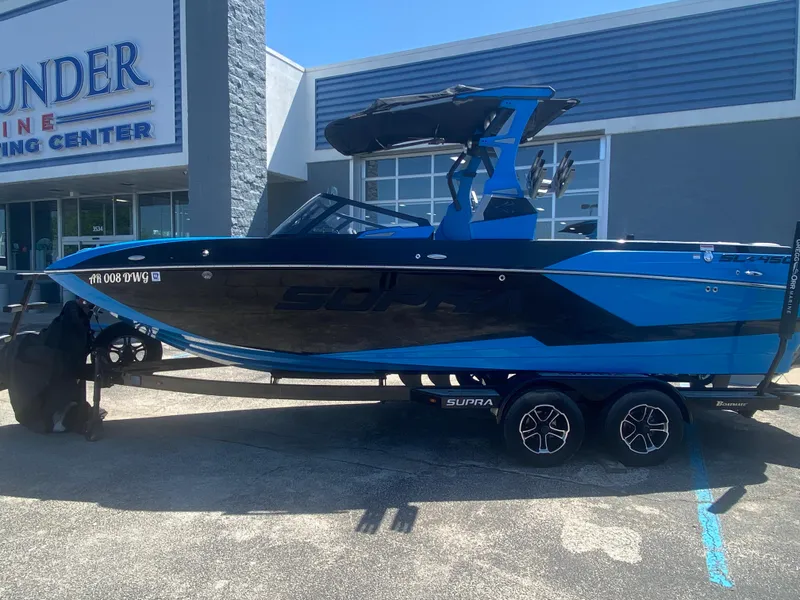 Slide: The Image of 2021 Supra SL 450 boat in blue and black on a trailer outside a marine center. - 2