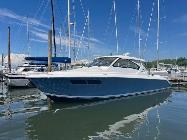 Slide: The Image of 2019 Pursuit DC 365 Dual Console boat docked in marina under clear blue sky. - 2