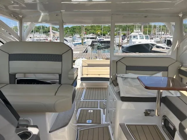 Slide: The Image of 2019 Pursuit DC 365 Dual Console interior with seating, table, and marina view. - 35