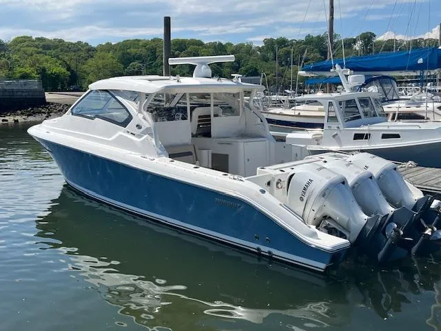 Slide: The Image of 2019 Pursuit DC 365 Dual Console boat docked in a marina, featuring twin outboard engines. - 6