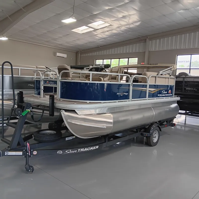 Slide: The Image of 2025 Sun Tracker Bass Buggy 16 XL Select pontoon boat in showroom on trailer. - 2