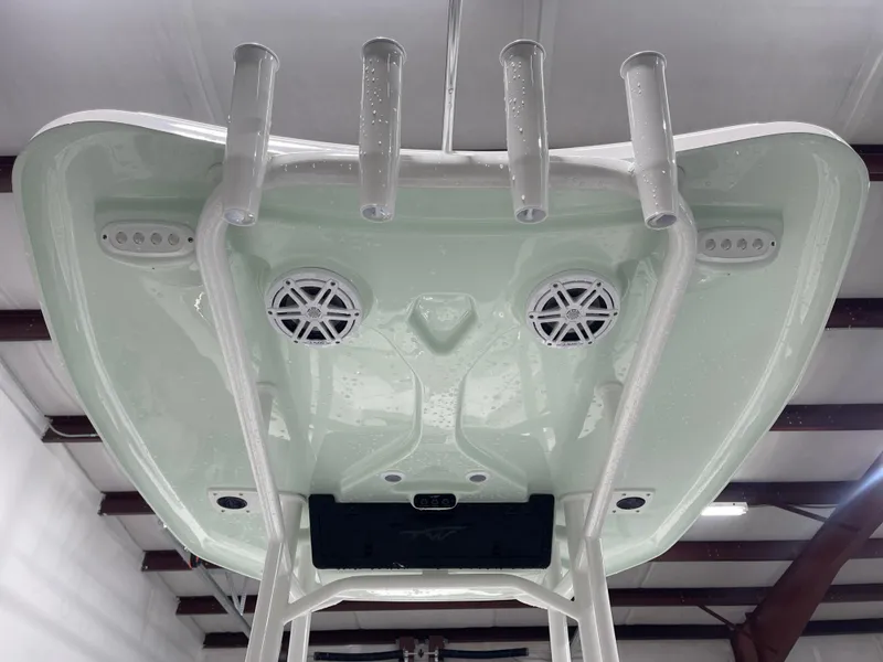 Slide: The Image of 2025 Tidewater 210LXF boat underside with speakers and rod holders in a warehouse. - 25