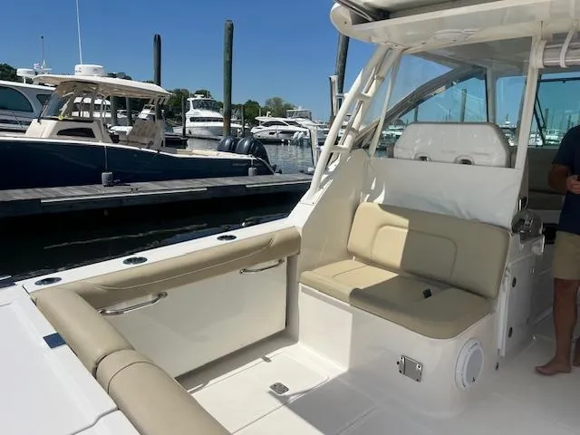 Slide: The Image of 2017 Pursuit DC 325 Dual Console boat interior with beige seating at marina. - 10