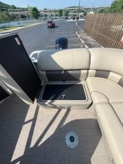 Slide: The Image of 2023 Sun Tracker Party Barge 20 DLX interior with seating and storage, parked near a river. - 8