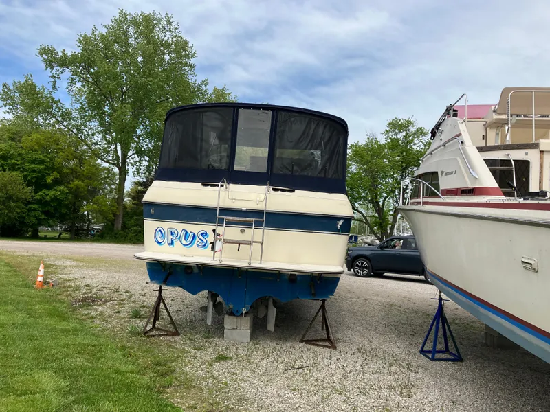 Slide: The Image of 1985 Cruisers 336 Ultra Vee boat on stands, parked outdoors, with trees in the background. - 1